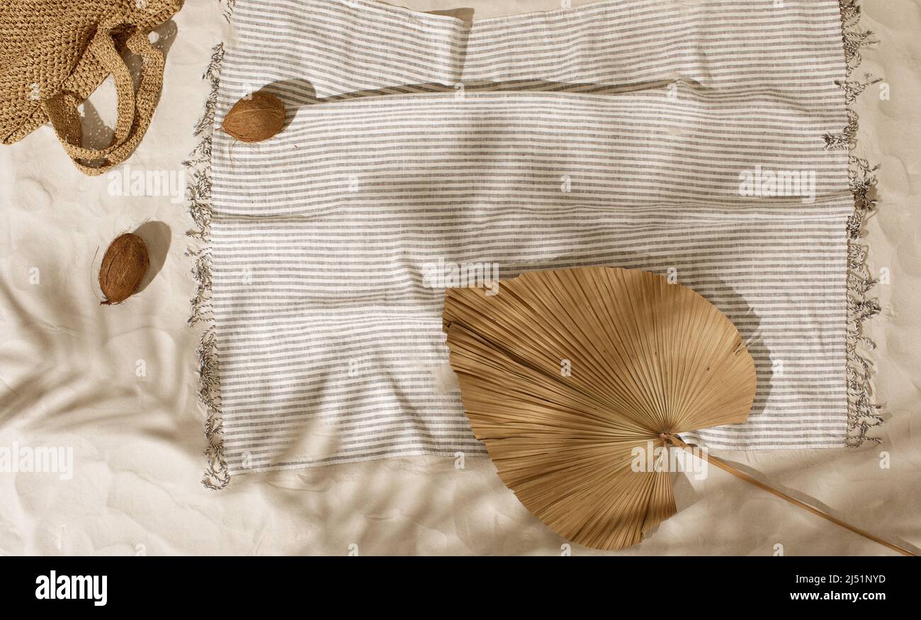 Striped linen beach towel, woven bag and two coconuts on sandy beach ...