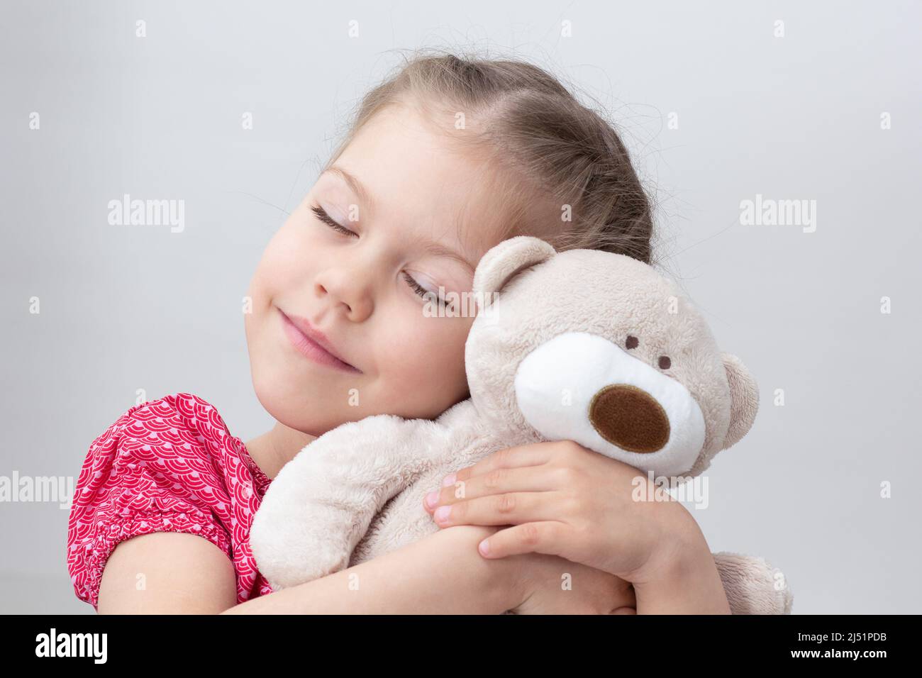 Happy child hugging teddy bear on white background caucasian little girl of 5-6 years in red with closed eyes Stock Photo