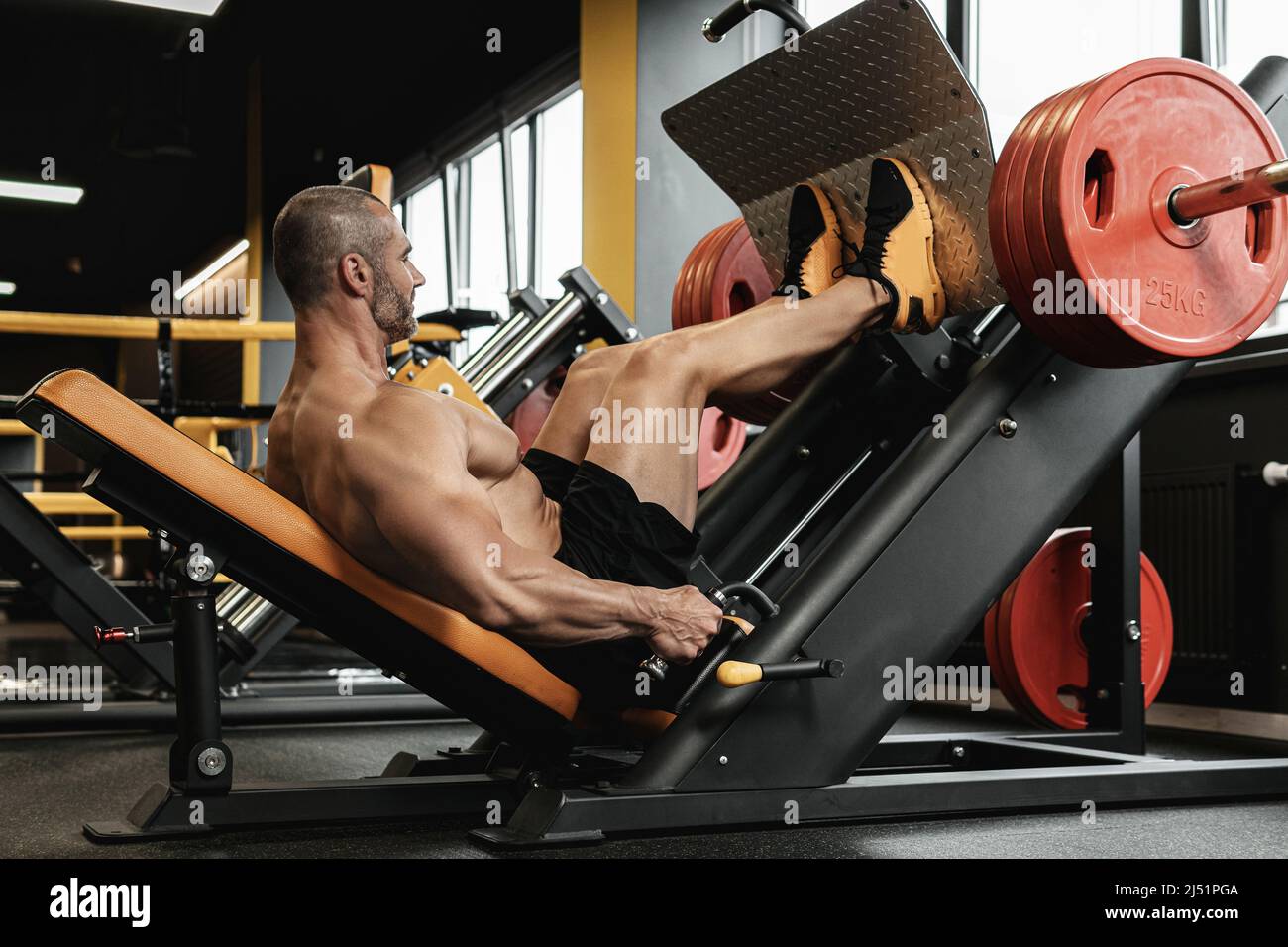 Strong and muscular bodybuilder doing a seated leg press exercise in a ...