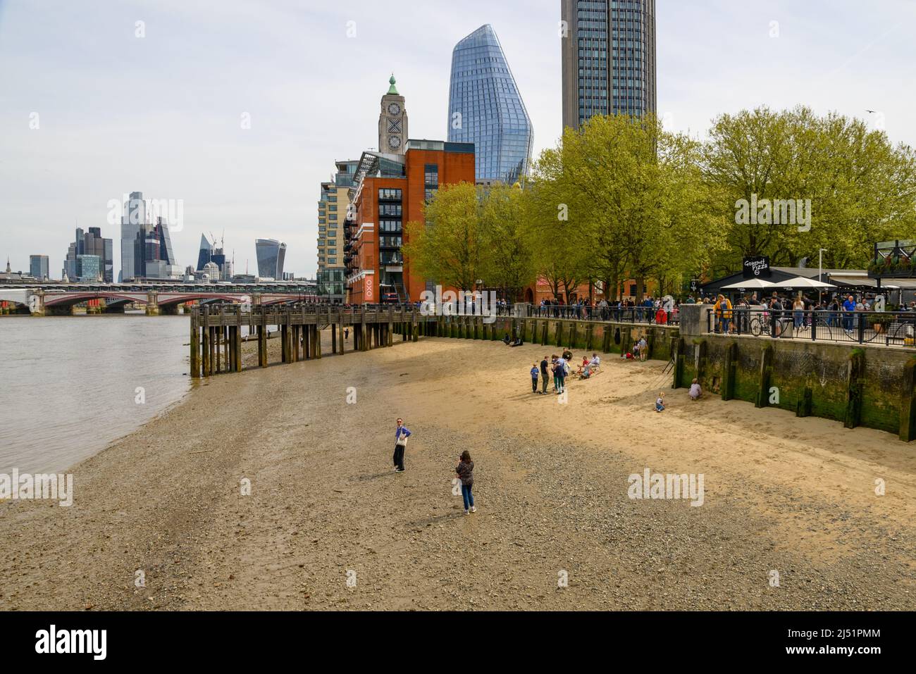 People on small sandy beach on the banks of The River Thames at low tide, South Bank, London, UK, April Stock Photo