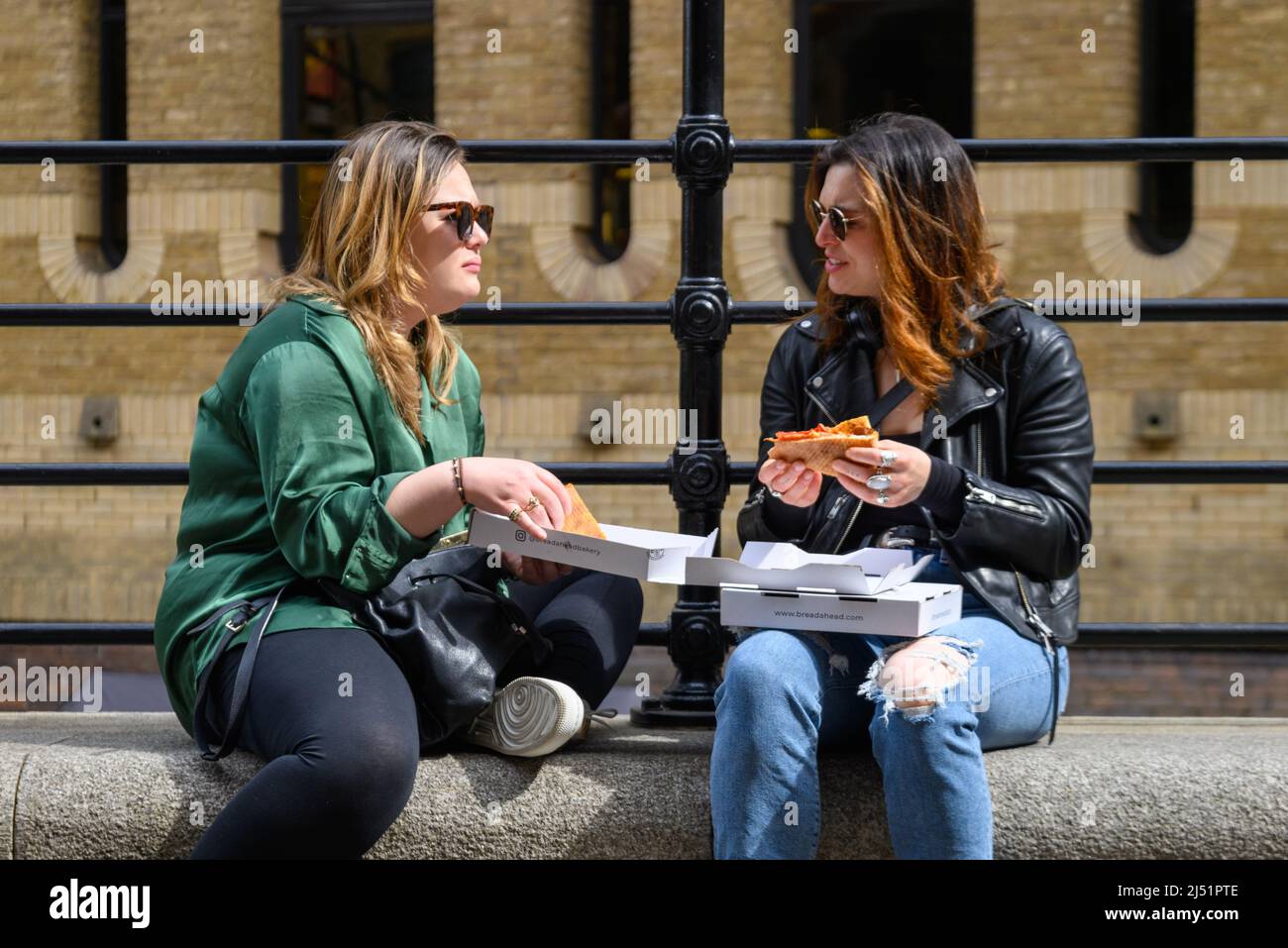 Two women chatting over pizza from a box at lunchtime outdoors, London, UK, April Stock Photo