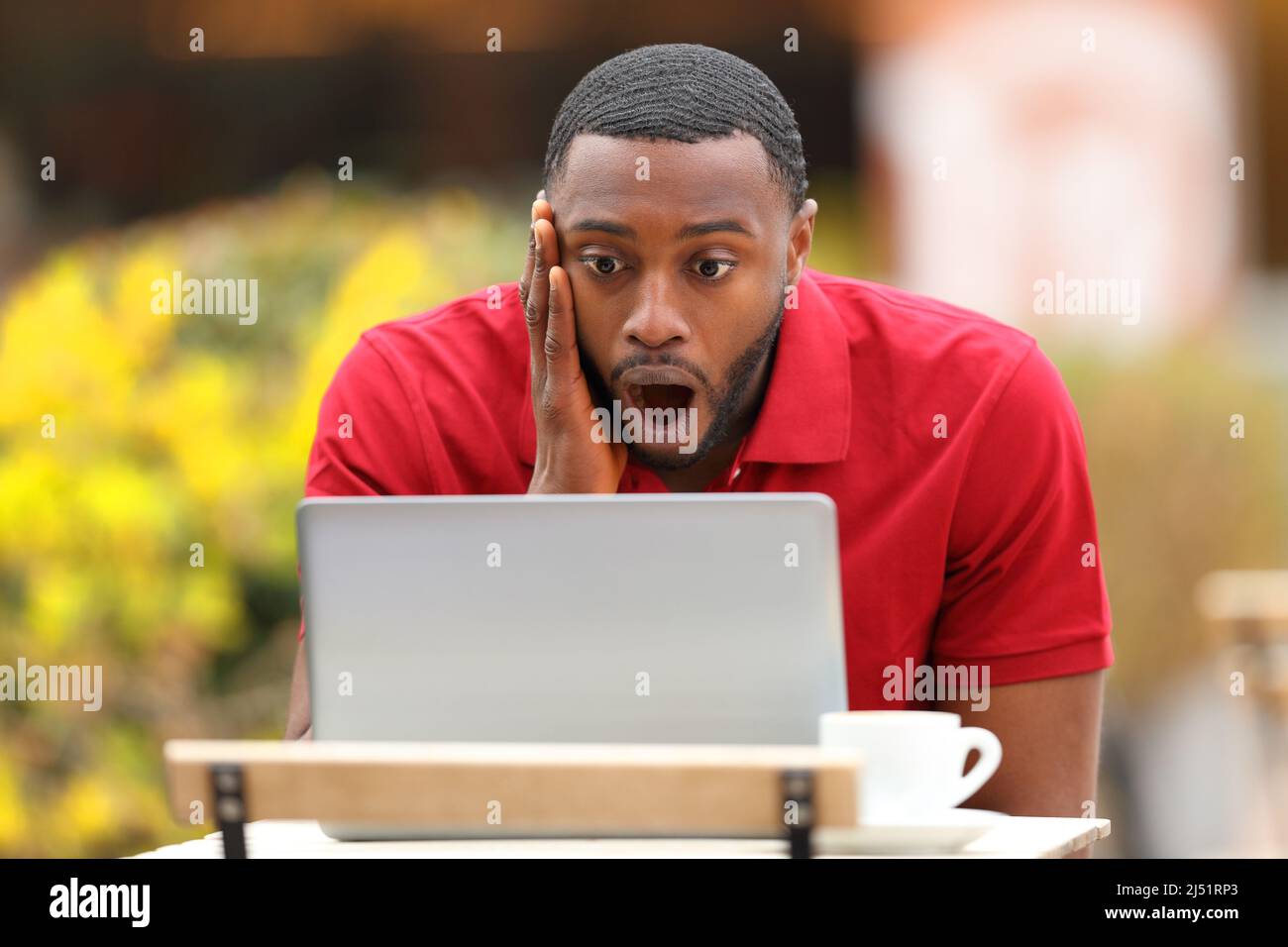 Front view portrait of a shocked man with black skin checking laptop in a coffee shop terrace Stock Photo