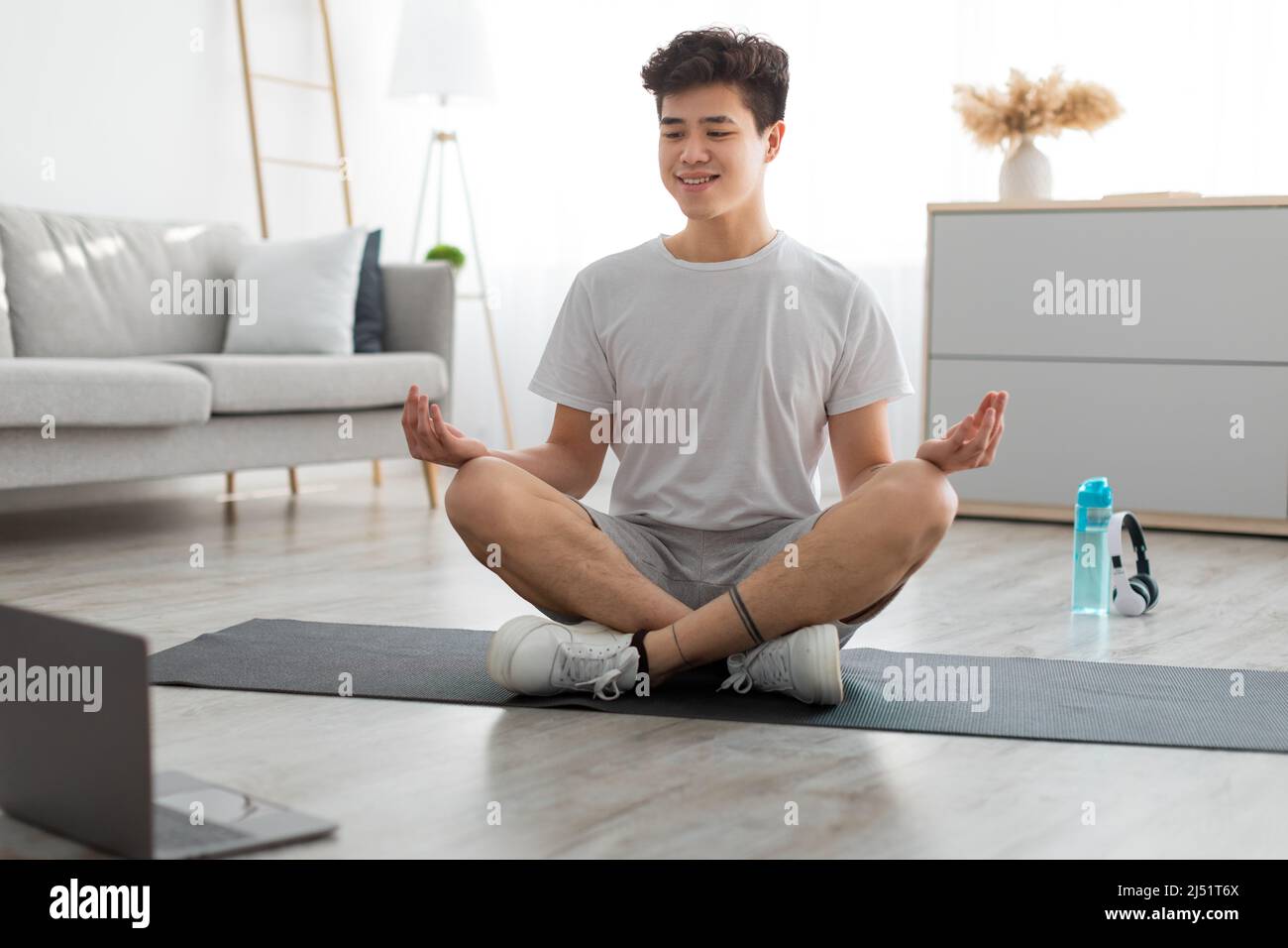 Asian man meditating in lotus position on mat with pc Stock Photo - Alamy