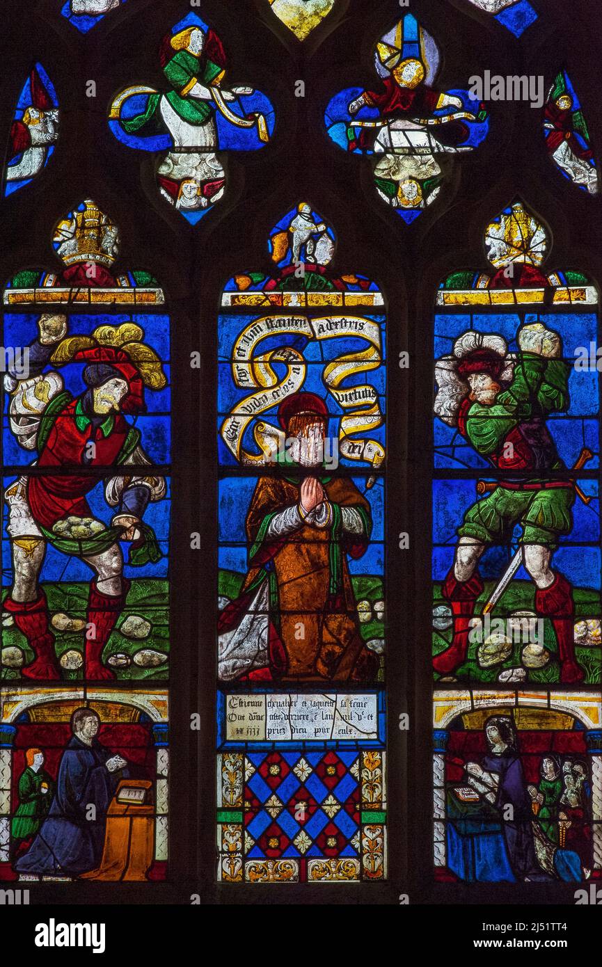 Blood streams down the face of Saint Stephen, the first Christian martyr, as he kneels in prayer while executioners in 16th century Renaissance dress hurl rocks at him from either side: vivid early 1500s Troyenne stained glass in the Église Saint-Rémi at Ceffonds, a village in the Champagne region of northeast France. Stock Photo