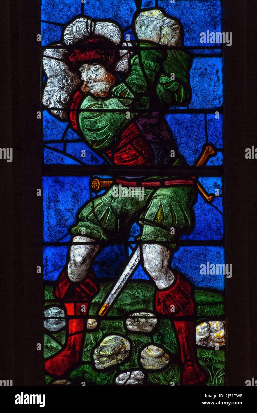 An executioner in colourful Renaissance costume hurls rocks at the first Christian martyr, Saint Stephen, in this vivid detail of early 1500s stained glass in the Église Saint-Rémi at Ceffonds, in the Champagne region of northeast France.  The colours are typical of 16th century glass made in the workshops at Troyes, the historic regional capital. Stock Photo