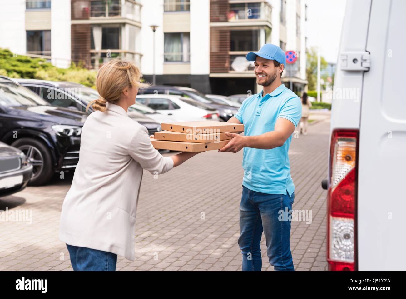 Professional delivery man wearing blue uniform delivers pizza to a woman client Stock Photo