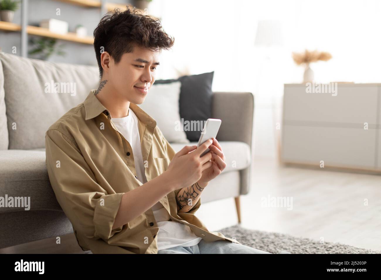 Smiling asian man using cellphone at home sitting on floor Stock Photo