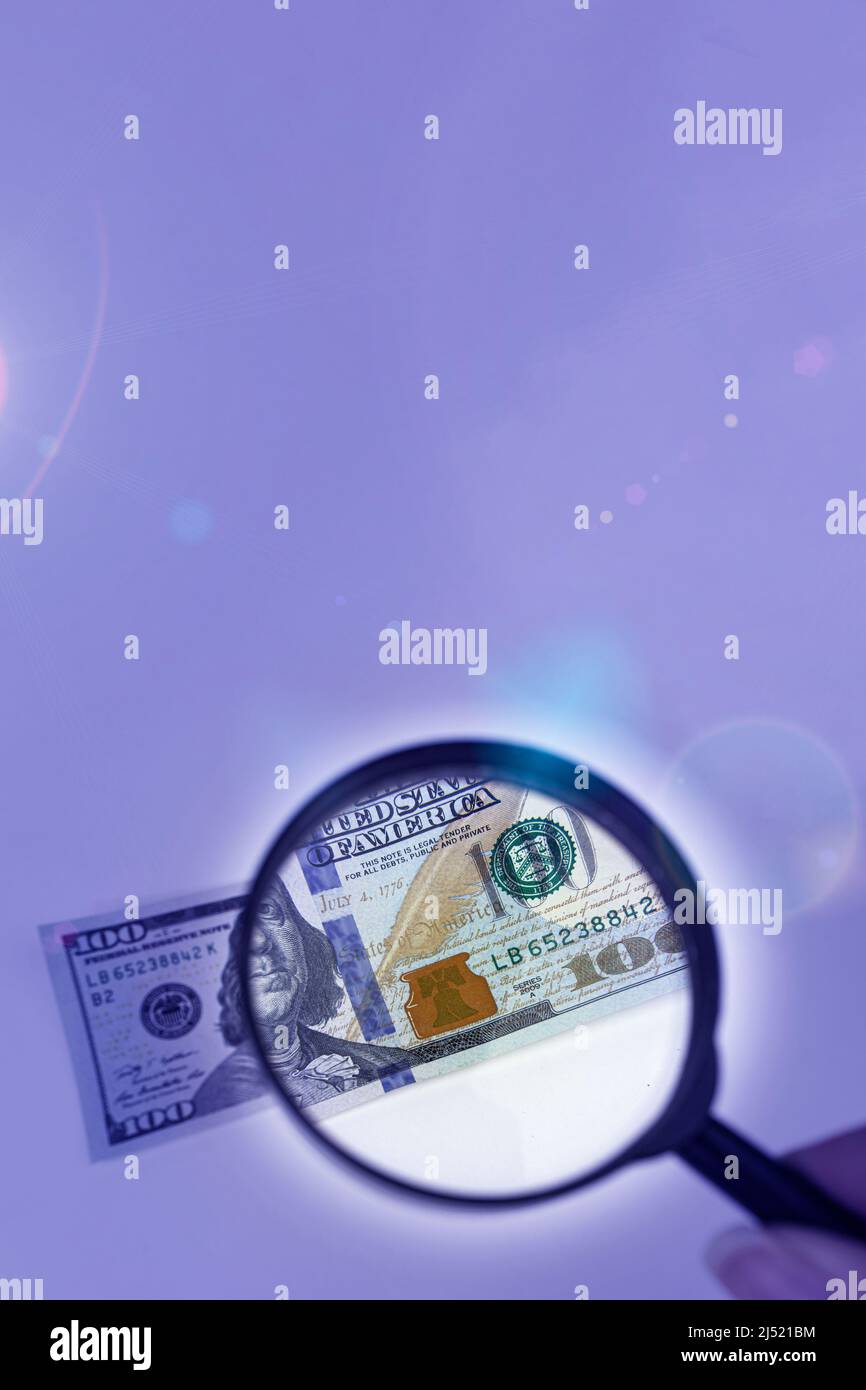 Magnifying glass on a pile of 100 dollar banknotes. Checking suspicious