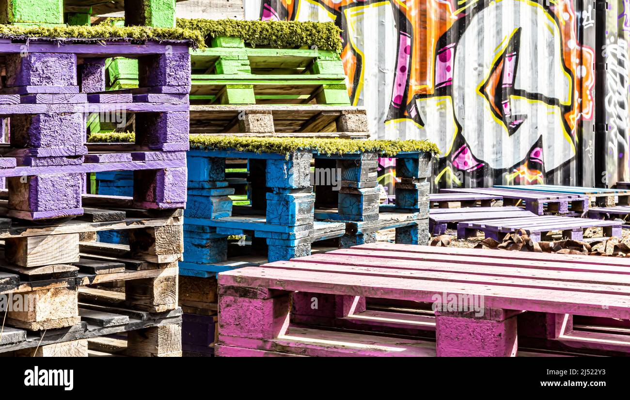 Pallets painted in various colours. In the background, a freight container covered in graffiti. Stock Photo