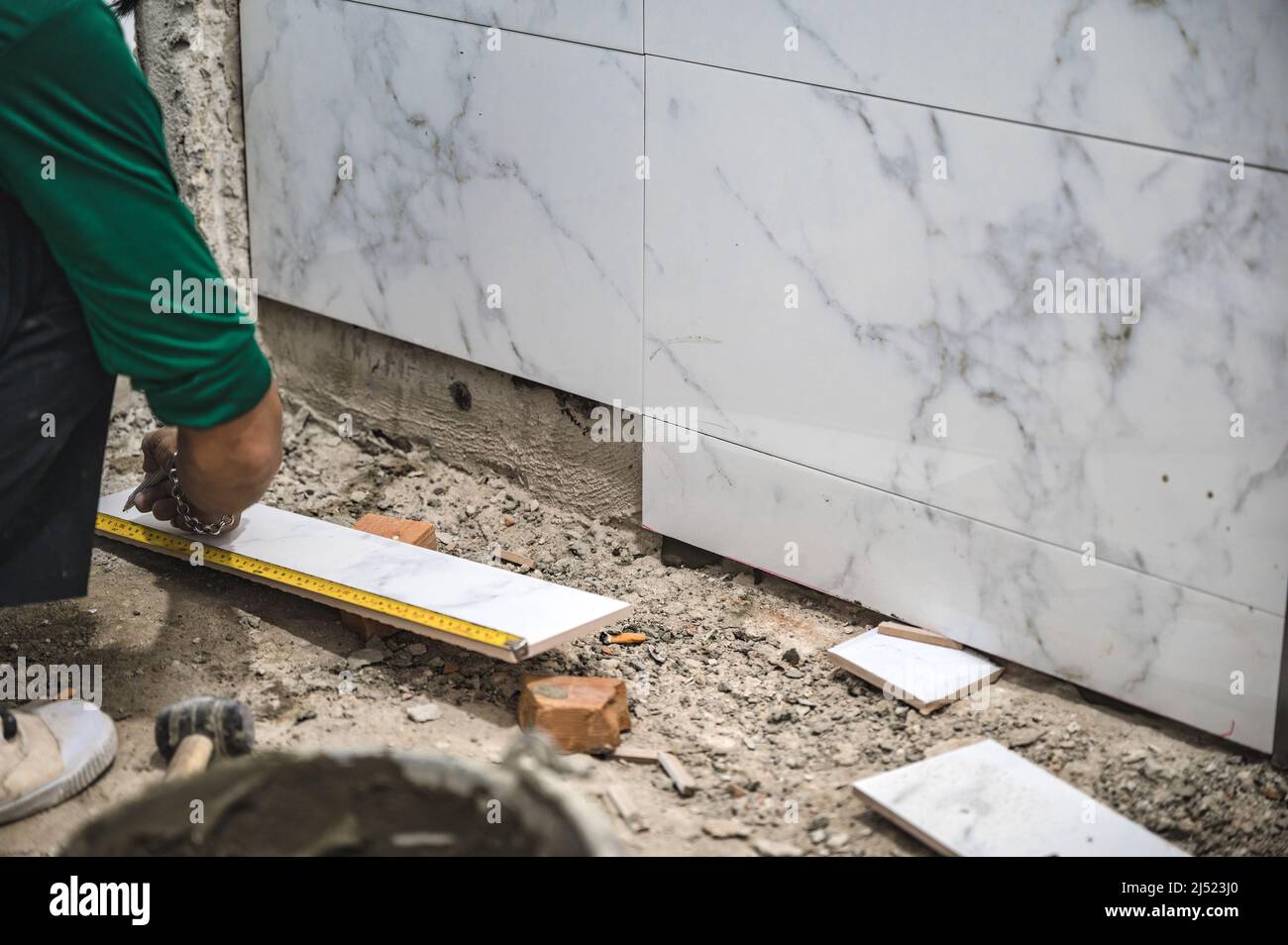 Male tiler using trowel laying marble tile with cement in bathroom. Housing development