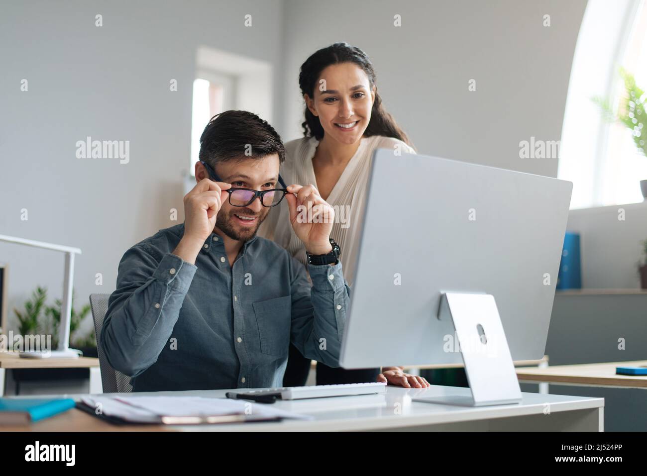Two happy colleagues working on startup project together, discussing ideas, using modern computer at open space office Stock Photo