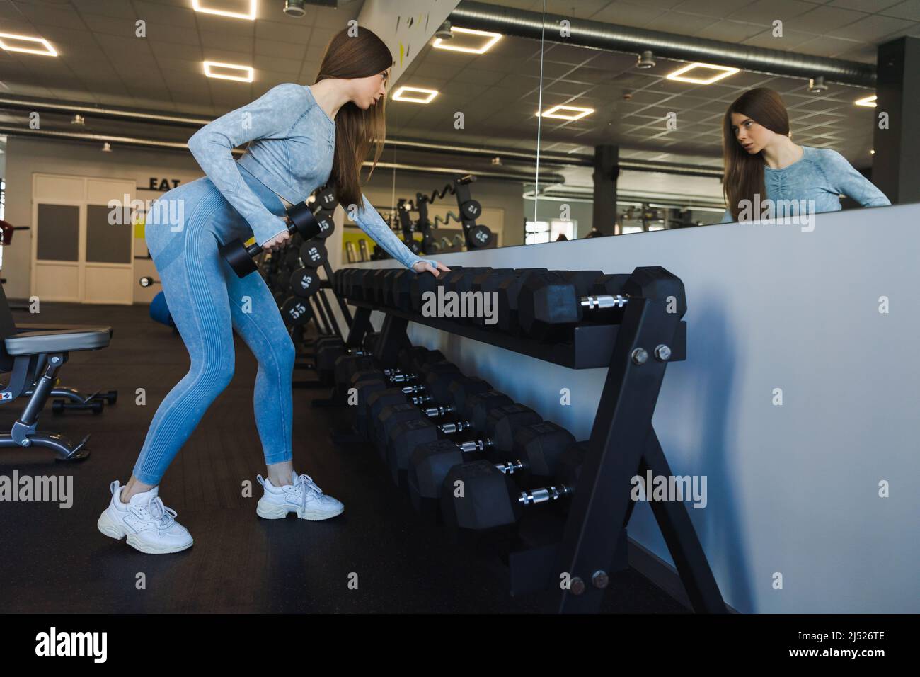 Fitness girl doing exercise with dumbbells and looking at her