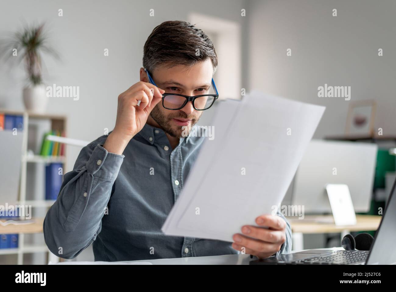 Concerned mature businessman in eyeglasses reading documents at workplace in office, checking annual reports Stock Photo