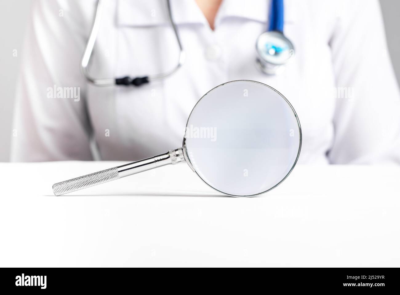 Doctor sitting at table with magnifier. Medical checkup, diseases prevention and diagnosis concept. Woman with stethoscope in lab coat. High quality photo Stock Photo