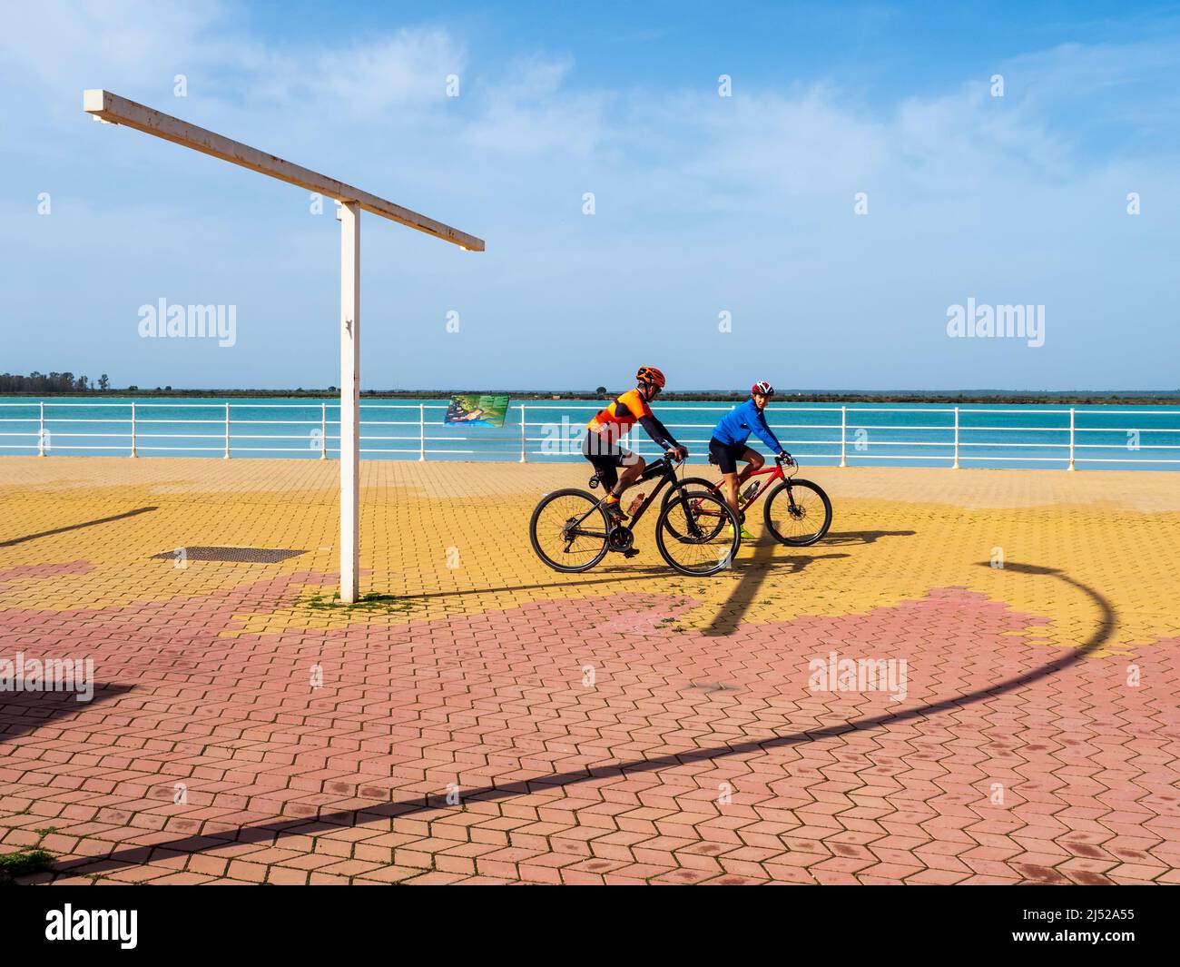 Young couple cycling along the Paseo de la Ría del río Odiel in Huelva on a sunny day. Stock Photo