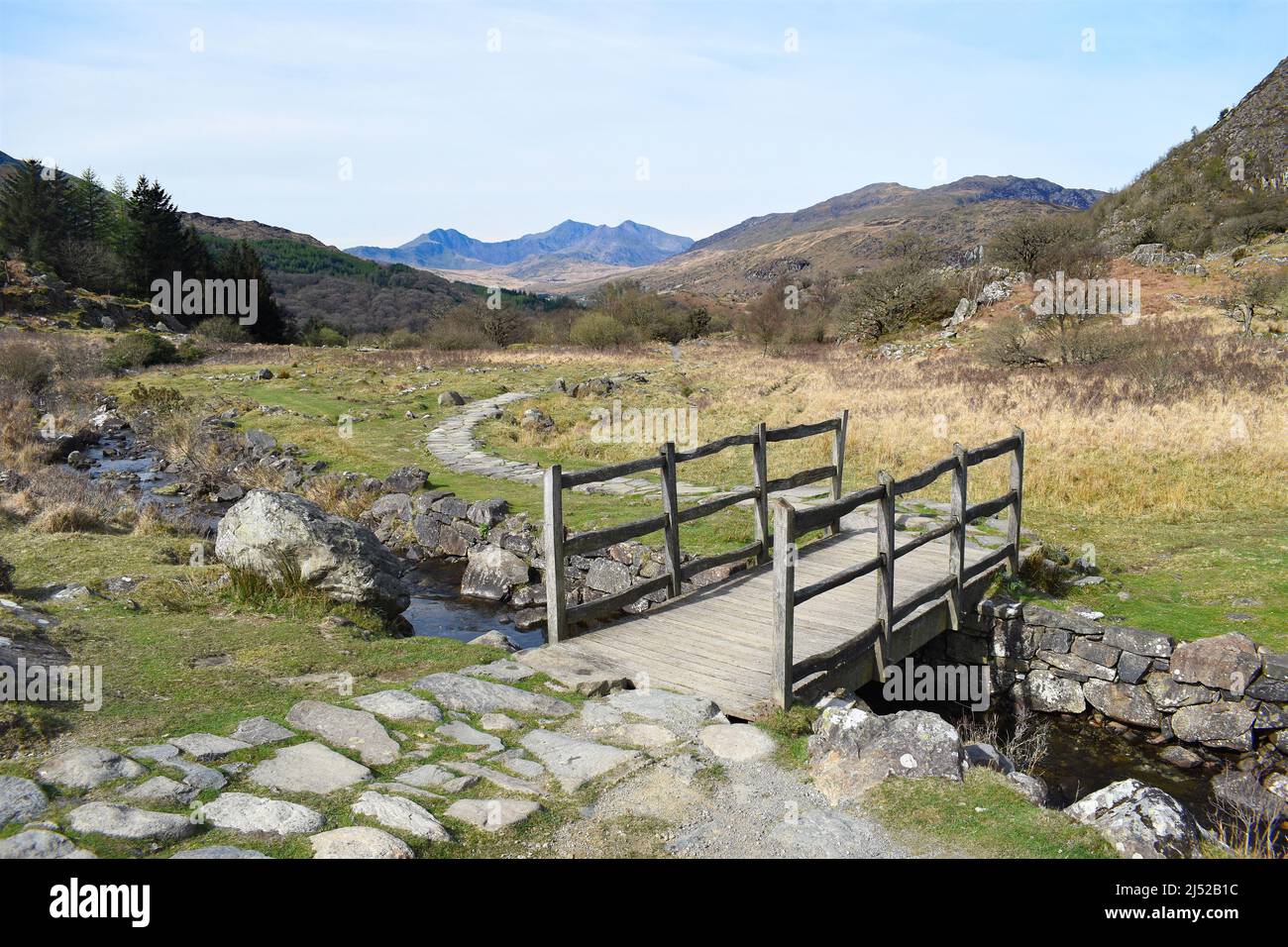 View of a public footpath bridge crossing a stream in Snowdonia, Wales, UK. In the background the mountain range including Mt Snowdon and Y Lliwedd. Stock Photo
