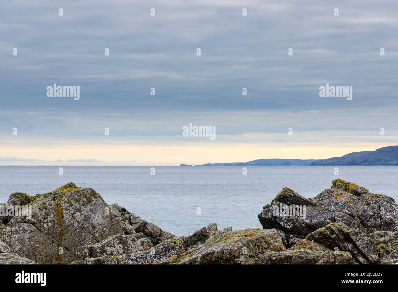 On an overcast but clear day, the coastline leads to the distant Strathay Point and lighthouse just visible on the horizon. Seen from near Skerray Bay Stock Photo