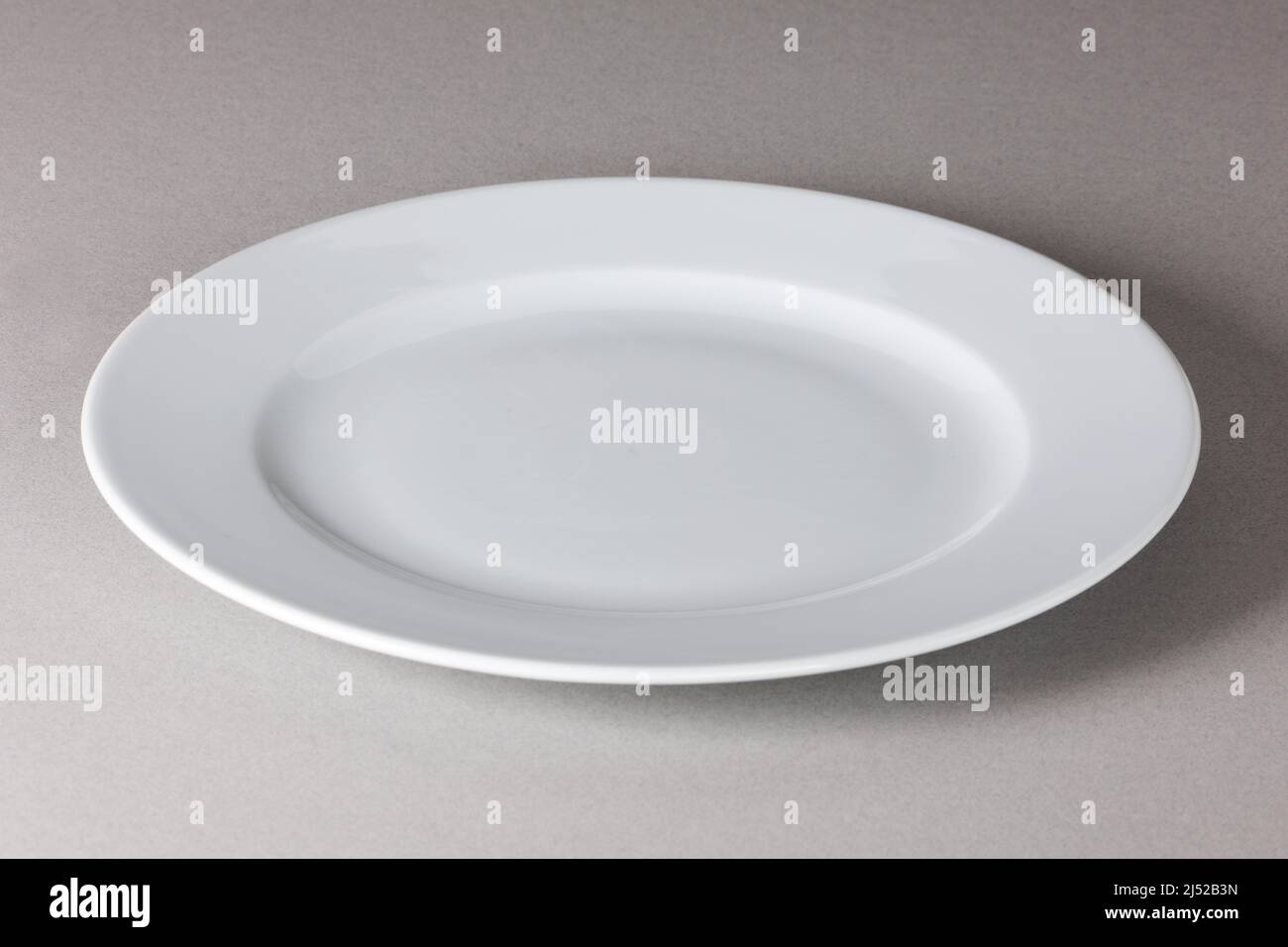 Raised view of a white dinner plate on neutral background with shadow Stock Photo