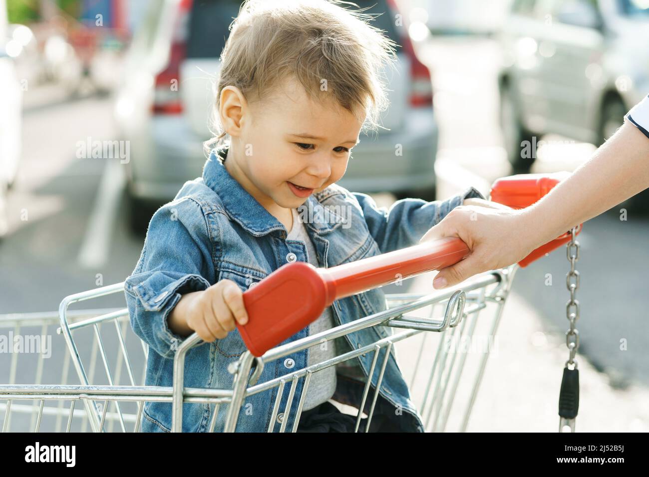 Cute little boy is sitting in a shopping cart in supermarket parking