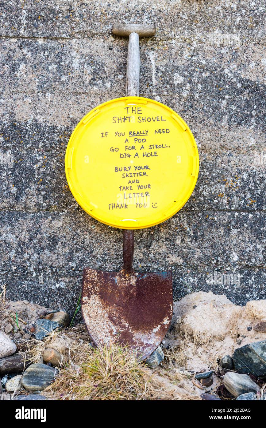 An old shovel propped against a wall with a notice for visiting travellers attached to it regarding litter and burying poo. Stock Photo