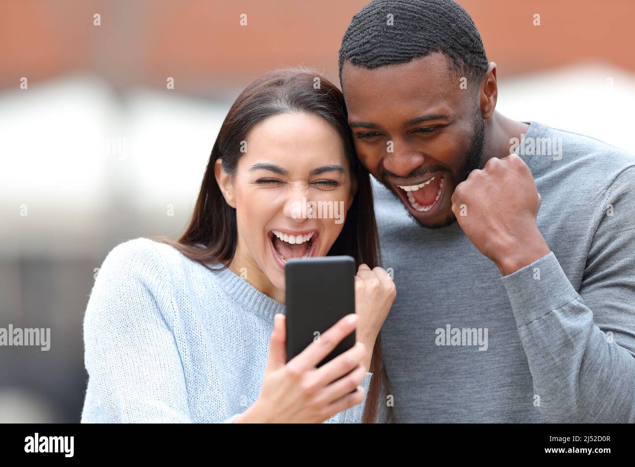 Excited interracial couple checking smart phone in the street Stock Photo