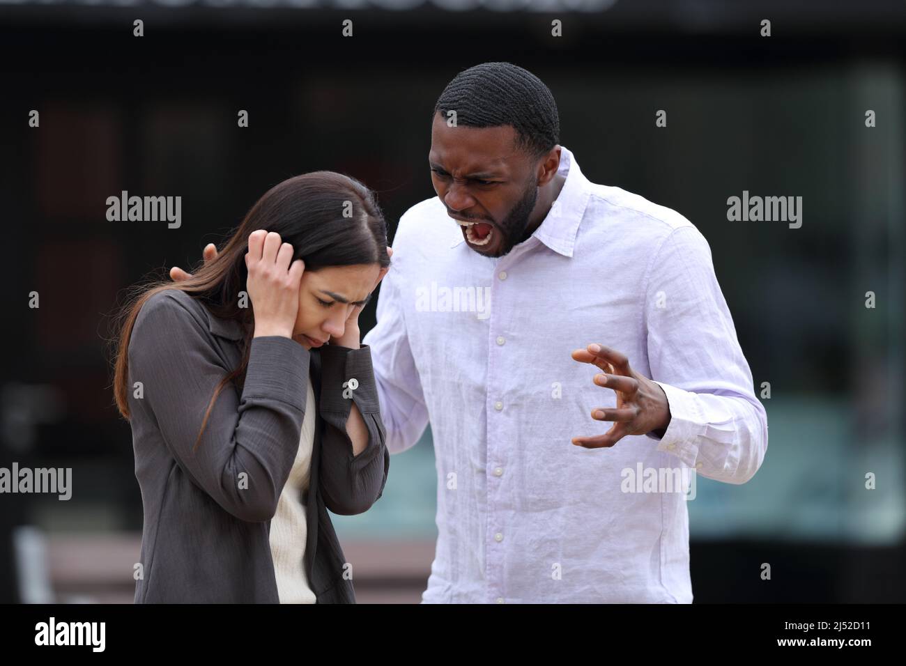 Angry man scolding and shouting to a scared woman in the street Stock Photo
