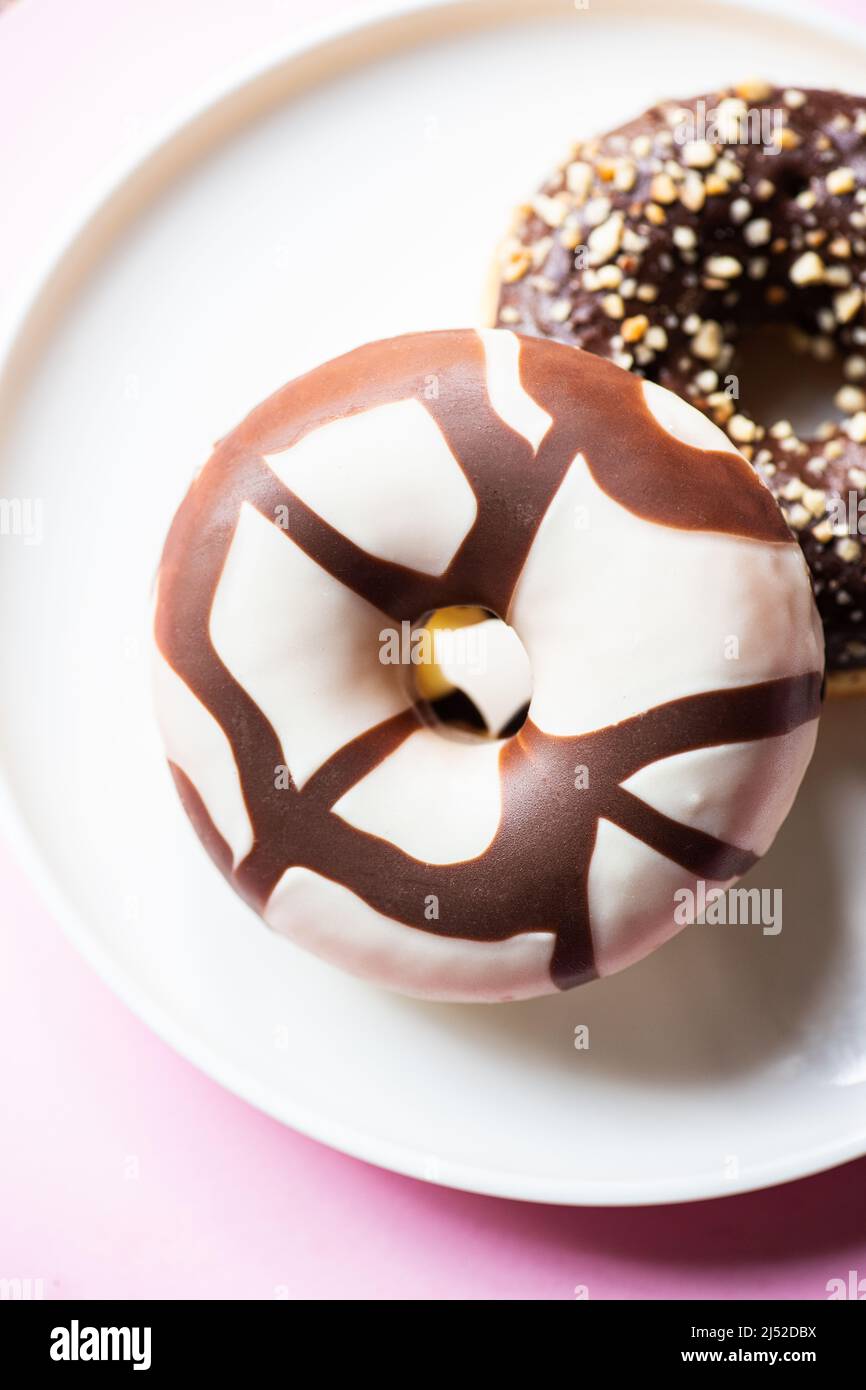 Two doughnuts with chocolate glaze and peanuts on a pink background. Close up. Stock Photo