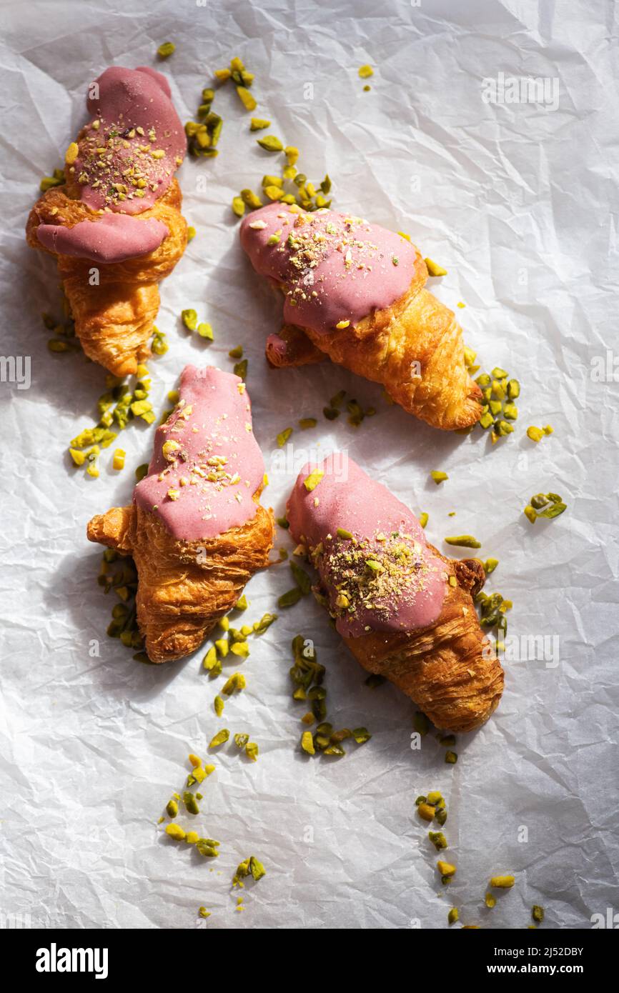 Mini-croissants with ruby chocolate and pistachios on a baking paper. Overhed view. Stock Photo