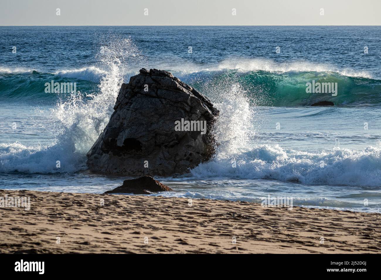 A wave splashes against a rock around sunset at Garapatta State Beach CA Stock Photo