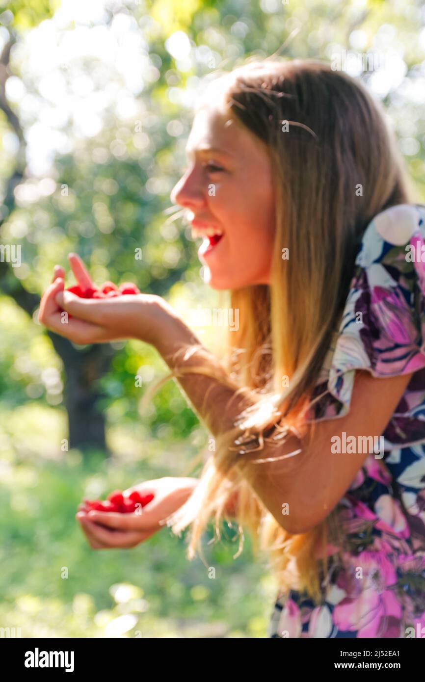 Defocus beautiful smiling teenage girl in dress smiling against green summer background. Abstract summer background. Teen girl holding raspberries Stock Photo