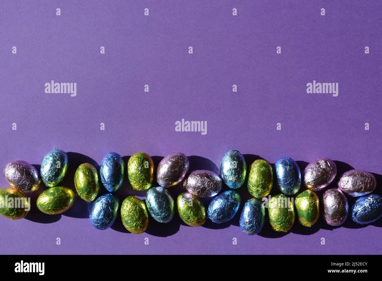 Foil wrapped chocolate Easter eggs isolate on purple background with copy space Stock Photo