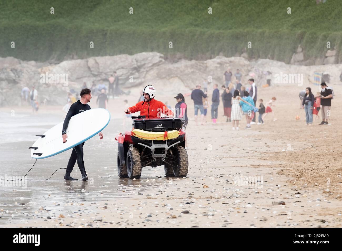 A RNLI Lifeguard offers advice to a surfer on a busy Fistral Beach, Newquay, UK. The lifeguards patrol on quad bikes at the popular surfing location Stock Photo