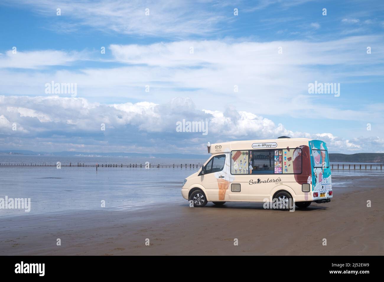 A traditional English ice cream van is parked waiting for customers on a sandy beach at Brean. A seaside resort in the South west of the UK Stock Photo
