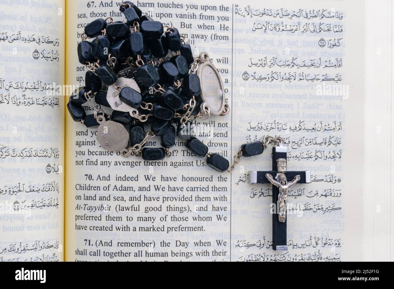 Catholic rosary beads sitting on top of an open Qu'ran. Stock Photo