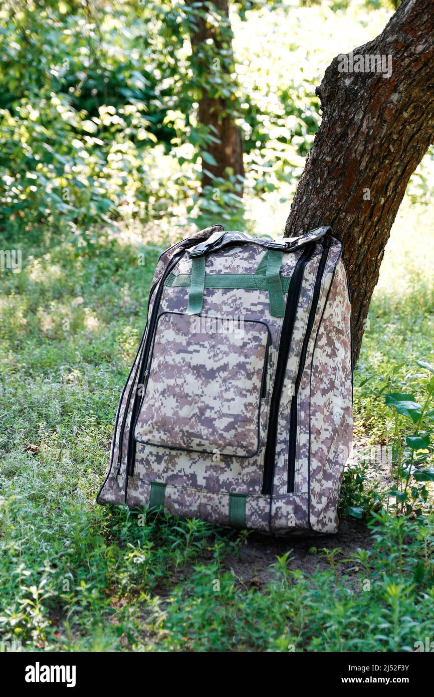 Defocus military backpack. Army bag on green grass background near tree. Military camouflage webbing material on a British army rucksack, backpack Stock Photo