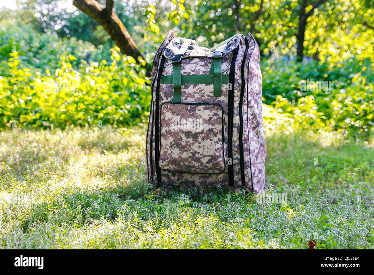 Defocus military backpack. Army bag on green grass background near tree. Military camouflage webbing material on a British army rucksack. Close-up Stock Photo