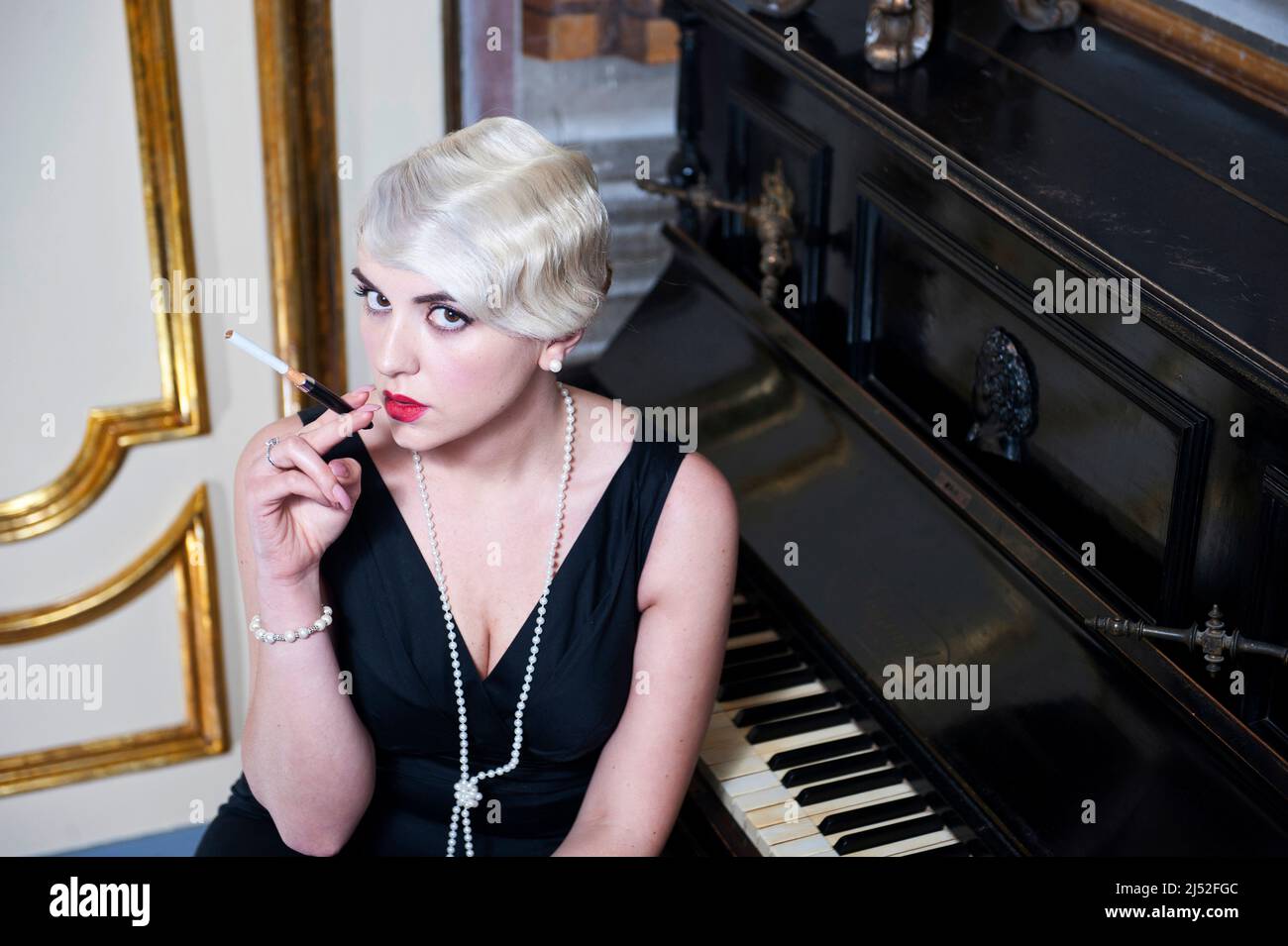 retro style elegant women smoking with mouthpiece next to a grand piano Stock Photo
