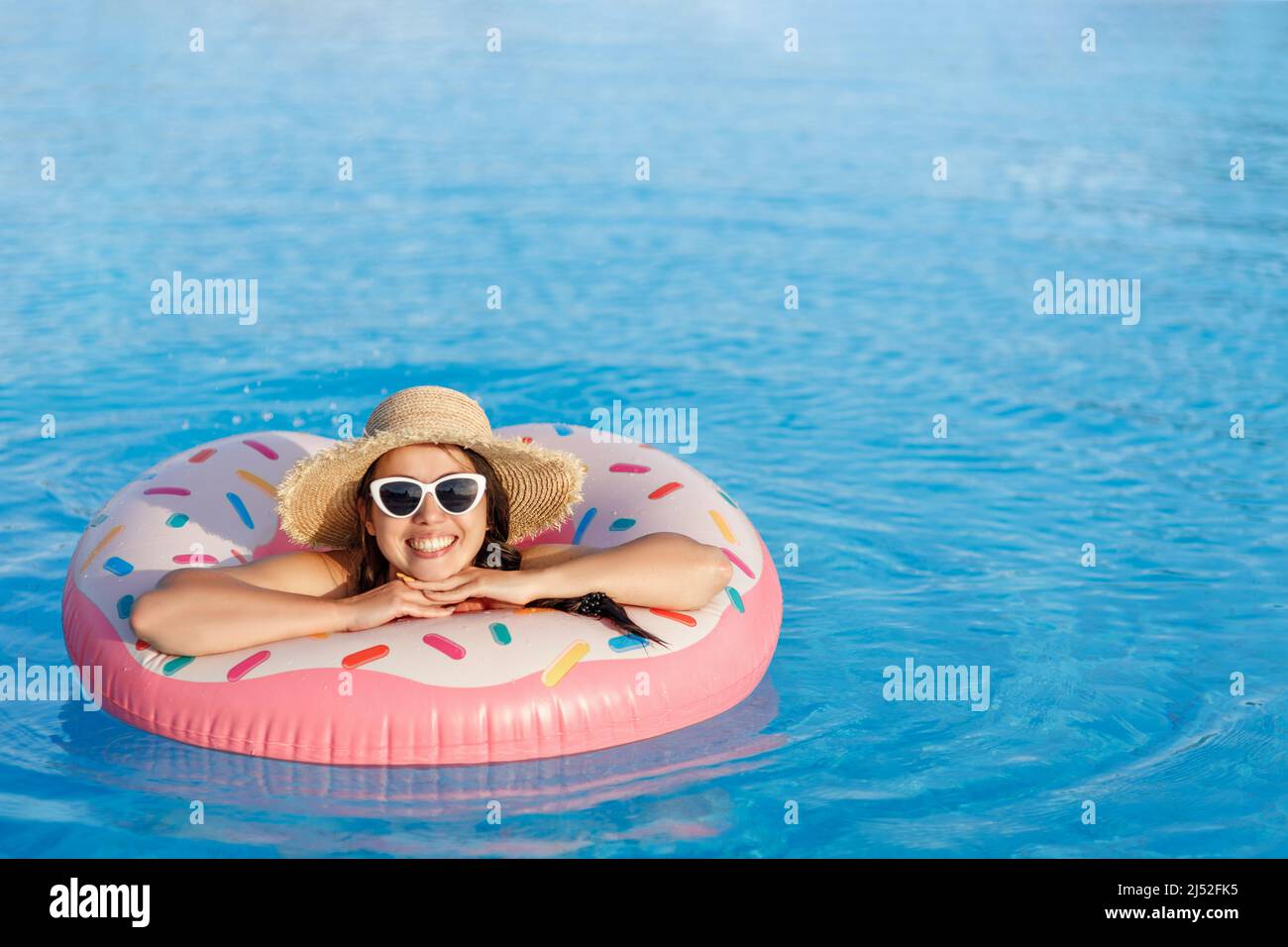 attractive young woman in straw hat and sunglasses relaxing on inflatable ring in swimming pool Stock Photo