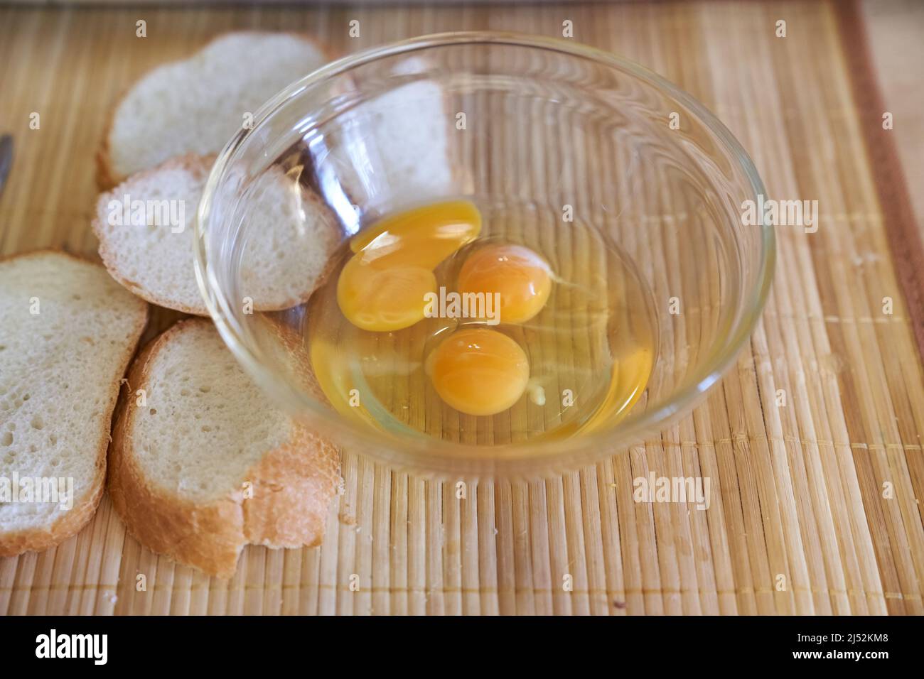 Three raw eggs in a clear glass bowl on the kitchen table with white bread. Step-by-step cooking of eggs for breakfast. High quality photo Stock Photo