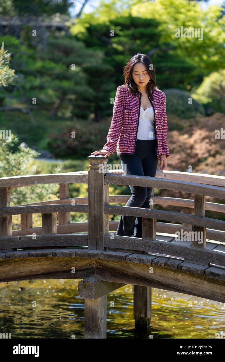 Young Woman in Casual Clothes on a Bridge Over a Japanese Koi Pond Stock Photo