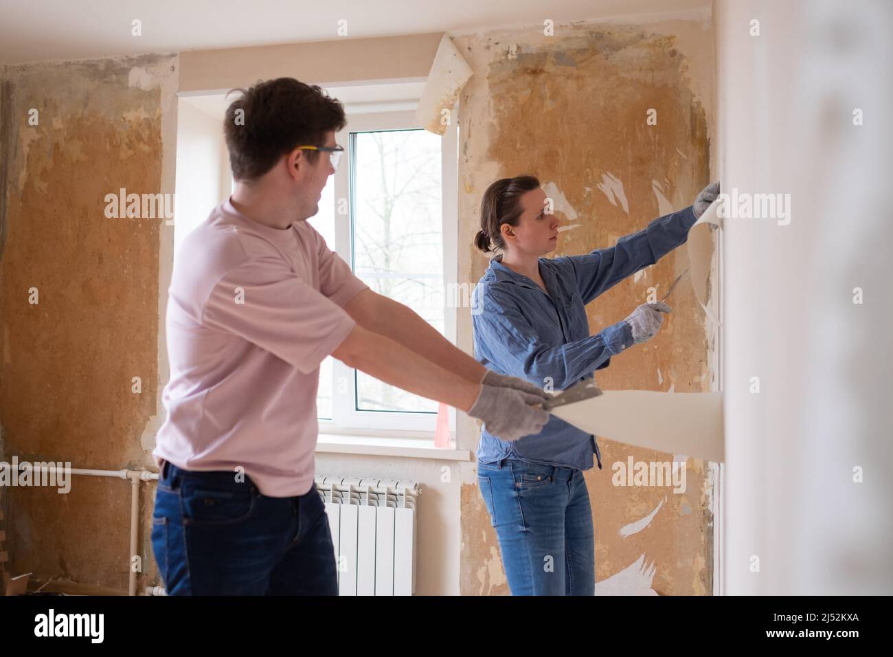 Young caucasian couple removing old wallpaper from walls preparing for
