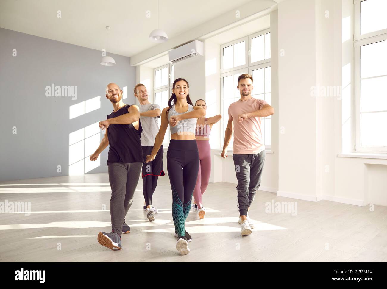 Group of happy young people doing sports exercises together while training in fitness studio. Stock Photo