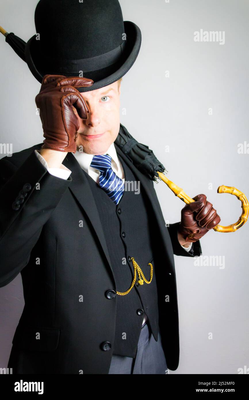 Portrait of British Businessman in Dark Suit and Leather Gloves Politely Doffing Bowler Hat in Courteous Greeting. Vintage Style of English Gentleman Stock Photo