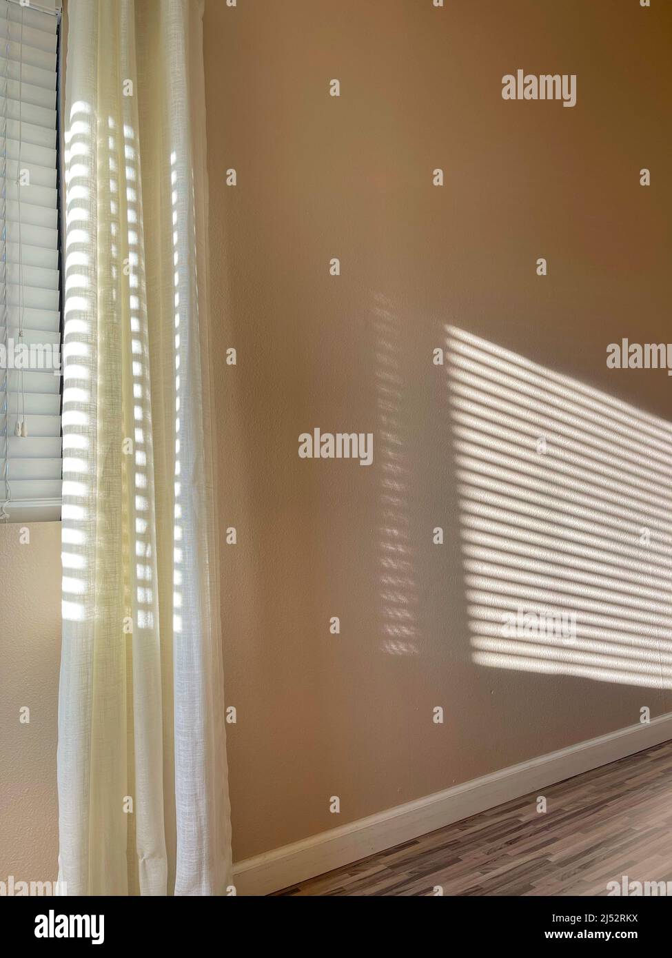 Sunlight streaming in through window blinds making a pattern on the wall Stock Photo