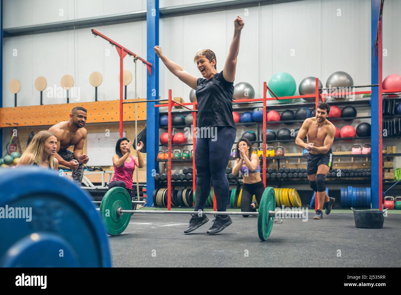 Happy woman celebrating her weightlifting achievement while her gym mates cheering her on Stock Photo