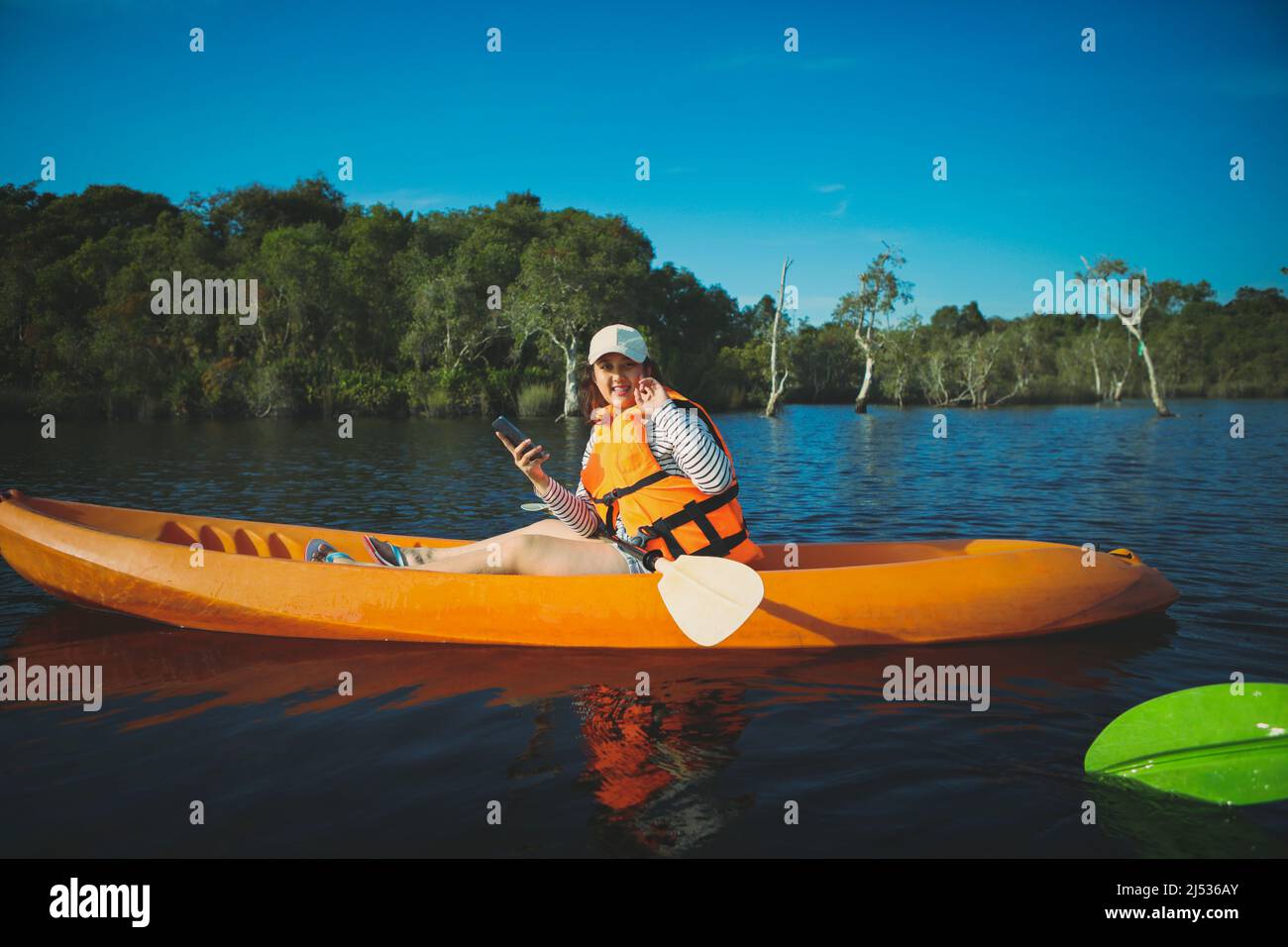 younger woman sitting in sea kayak and holding smartphone in hand Stock Photo