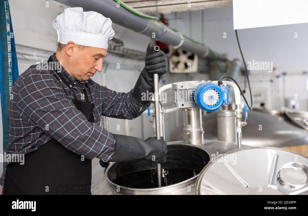 Skilled brewer mixing raw materials in fermentation vessel in brewery