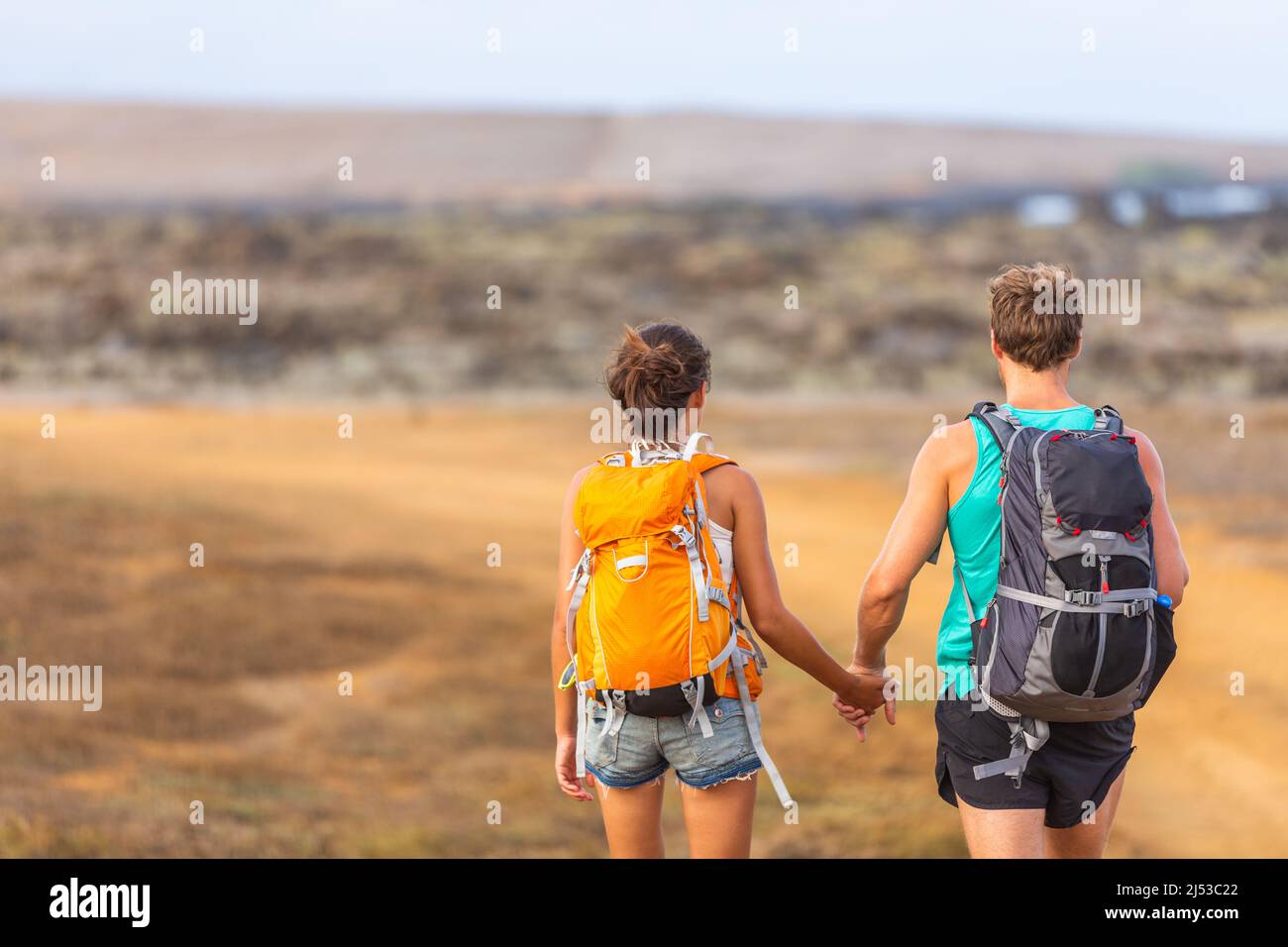 Hikers couple tourists walking together with backpacks holding hands walking in love. Young lovers travelers on travel adventure trek hike wanderlust Stock Photo