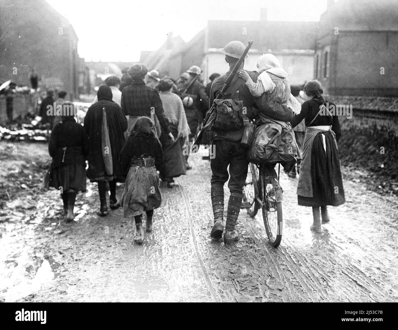 British soldiers arriving in a village in France. They are surrounded by women and children. One soldier has lifted a young girl onto his bicycle. T Stock Photo
