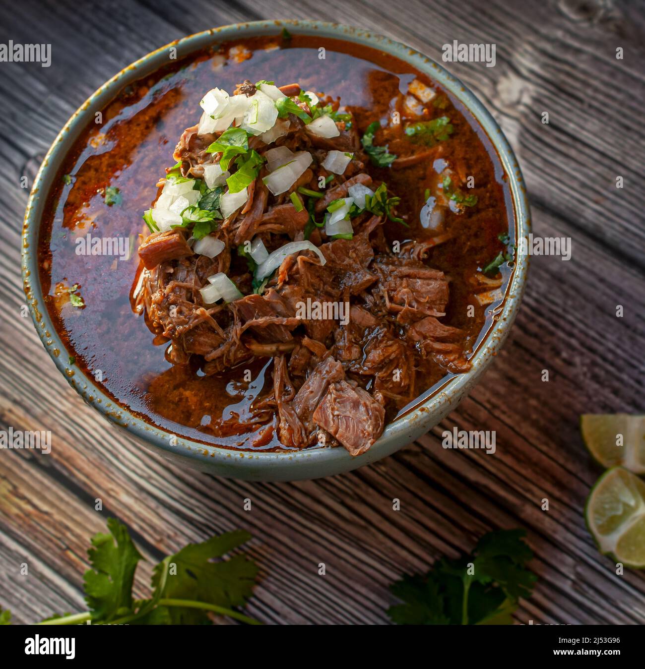 A bowl of BIRRIA or BARBACOA, a traditional Mexican dish with lemons and  cilantro on the side over a wooden table Stock Photo - Alamy